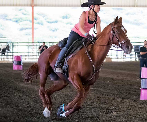 Dawn Champion riding her brown horse wearing Scoot Boots in a barrel racing course